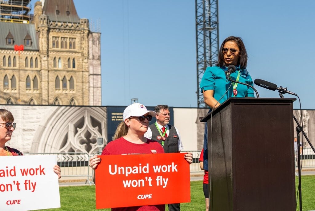 A labour leader standing at a podium in front of Parliament Hill